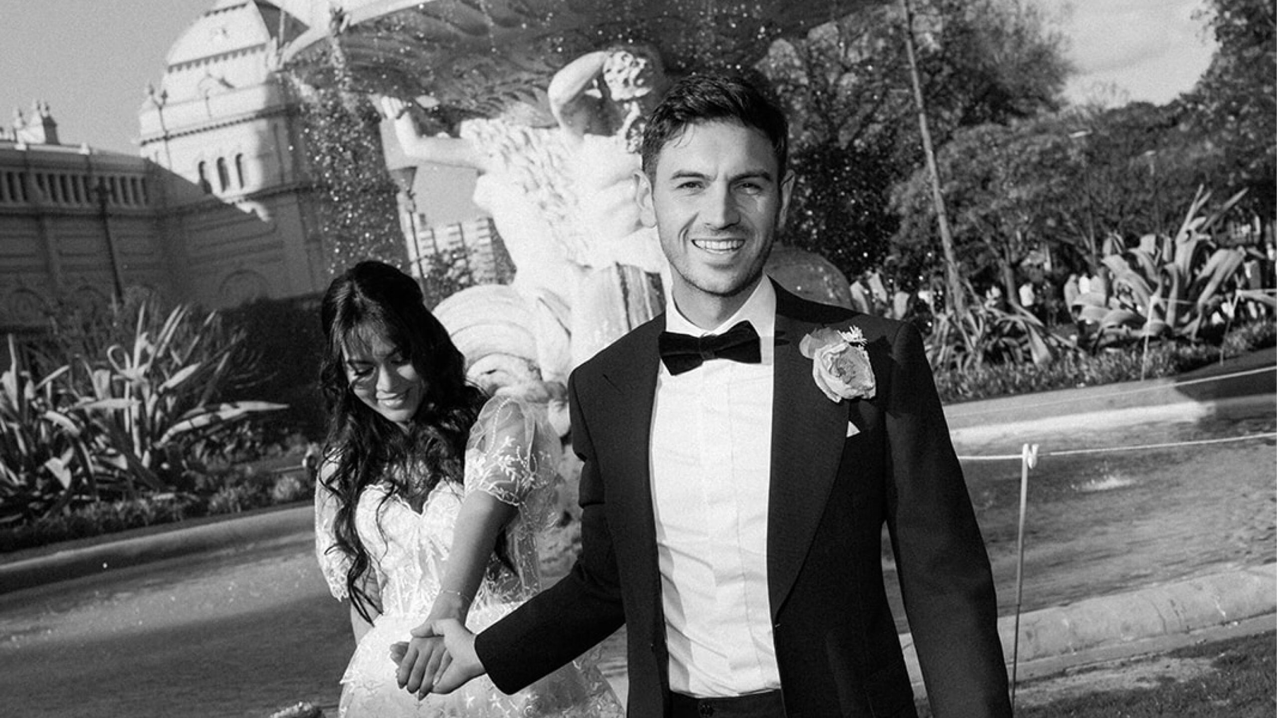 Newlywed couple by the water fountain in Carlton Gardens, Melbourne, captured by Art of Grace, showcasing their wedding day joy and elegance.